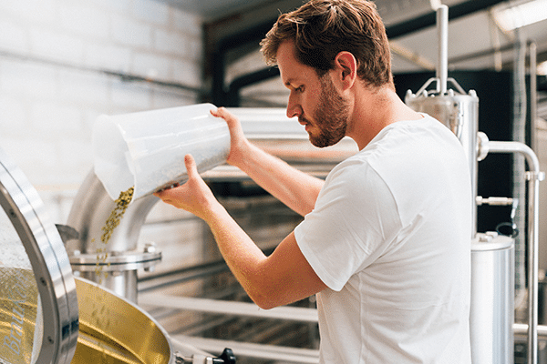 Formation-Titre-Brasseur-niveau-3-600×400 Brasseur professionnel versant du malt dans une cuve de brassage